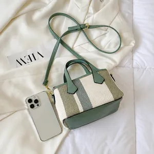 Detail shot of striped canvas bucket bag with green leather strap next to a smartphone