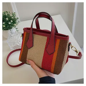 Detalle de un bolso tote de lona a rayas con adornos de cuero rojo y herrajes dorados