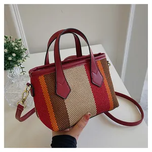 Detalle de bolso tote tejido a rayas de colores con asas de cuero rojo y herrajes dorados