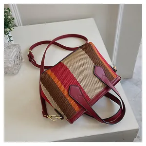 Detalle del bolso de cubo tejido a rayas coloridas con asa y correa de cuero rojo oscuro