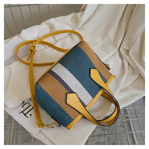 Detalle del bolso tipo cubo de lona con rayas azules y asas de cuero amarillo