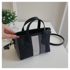 Detalle del bolso tipo cubo de lona con rayas verticales blancas y negras y asas de cuero