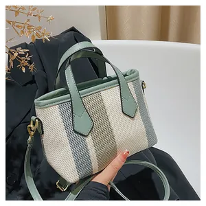 Detalle de bolso saco de lona a rayas con ribete de cuero verde y herrajes dorados