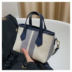 Detalle de mini bolso tote de lona a rayas azules y blancas con asas de cuero y ganchos