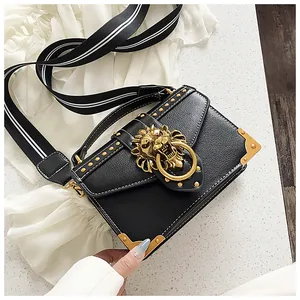 Detail of black pebbled leather crossbody bag with golden lion head buckle and rivets