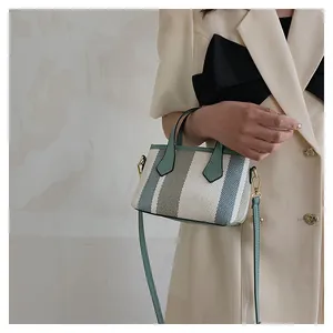 Detalle de bolso cubo de lona a rayas tricolores con asa verde menta y herrajes de oro