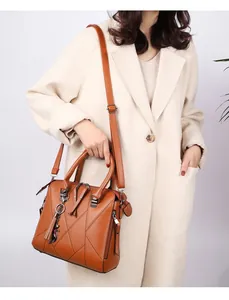 Detail of tan leather handbag with tassel charm held by a model in a beige wool coat