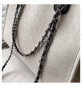 Detail der beigen Canvas-Beuteltasche mit eleganter Metallkette und Lederriemen