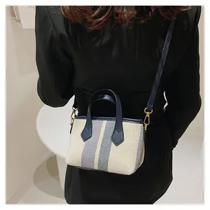 Detalle del pequeño bolso tipo cubo de lona con rayas azules y correa ajustable