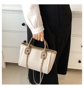 Detail der cremefarbenen Web-Beuteltasche mit braunem Lederbesatz und Metall-Kettenriemen