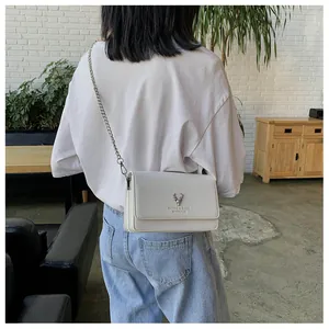 Gros plan du sac à bandoulière avec logo cerf argenté sur cuir texturé blanc élégant