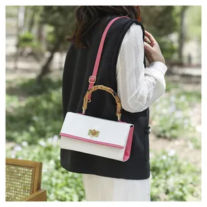 Sac à main bicolore à motif crocodile avec poignée en bambou porté en extérieur par un mannequin