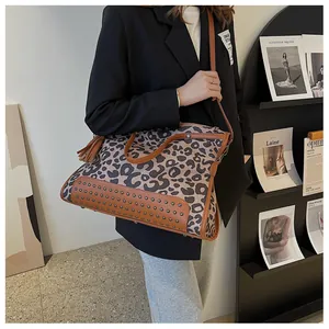 Détail d'un grand sac léopard avec rivets et poignées en cuir marron porté à l'épaule
