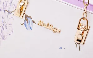 Detail of golden metal logo and floral print patterns on the elegant white shoulder bag