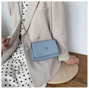 Détail du sac bandoulière bleu clair avec logo cerf argenté et fine chaîne en métal