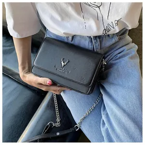 Détail du sac à bandoulière noir texture litchi avec logo cerf argenté sur un t-shirt blanc