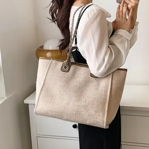 Borsa a secchiello beige con tracolla a catena e finiture in pelle marrone su modella
