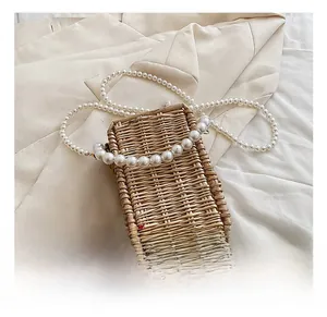Detail view of woven straw mini bag featuring decorative white pearl chain and natural texture