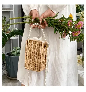 Straw woven box bag featuring pearl handle and shoulder strap held by a model