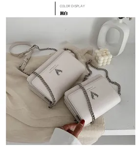 Détail d'un sac bandoulière blanc cassé avec tête de cerf en métal et chaîne