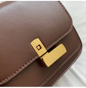 Détail d'un fermoir en métal doré sur un sac à bandoulière carré en cuir marron texturé
