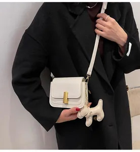 Gros plan d'un sac à bandoulière carré blanc avec breloque chien et fermoir doré