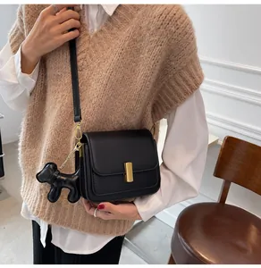 Chic sac bandoulière noir en cuir avec un charmant pendentif chien sur un modèle.