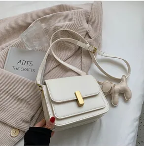 Détail d'un petit sac carré blanc minimaliste avec un charme de chien et fermoir doré.