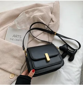 Gros plan d'un sac bandoulière en cuir noir avec un pendentif chien sur un blazer beige