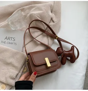 Détail d'un petit sac bandoulière marron avec fermoir doré et breloque en forme de chien.