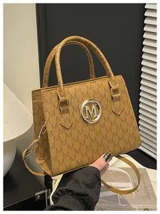 Dettaglio della borsa marrone con motivo M ripetuto e logo in metallo dorato circolare