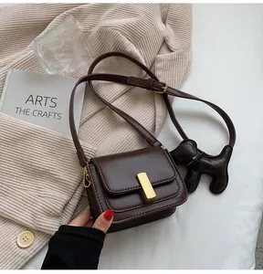 Gros plan d'un sac bandoulière en cuir marron avec boucle dorée et breloque chien.