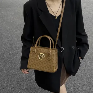 Borsa a mano marrone con monogramma M e logo dorato su modella con blazer nero