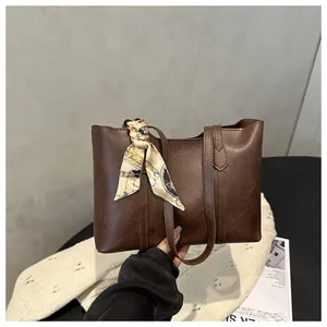 Detail einer dunkelbraunen Tragetasche aus Leder mit Kieselstruktur und beige Seidenschal