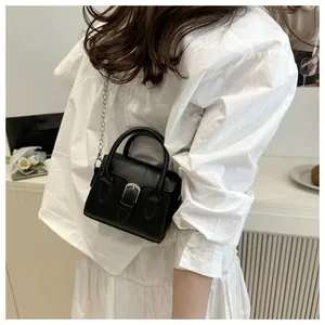 Detail of a chic black mini leather bag with silver buckle and chain on a model
