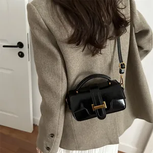 Classic black crossbody bag with gold buckle on a stylish model in a brown blazer