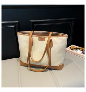 Gros plan du sac fourre-tout en toile beige avec bordure en cuir brun et logo gaufré