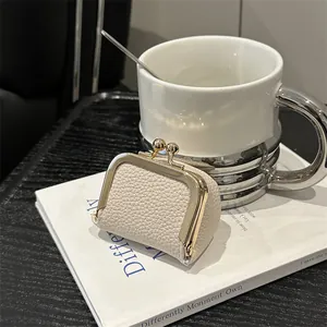 Mini porte-monnaie en cuir crème avec fermoir doré pour bijoux sur un livre