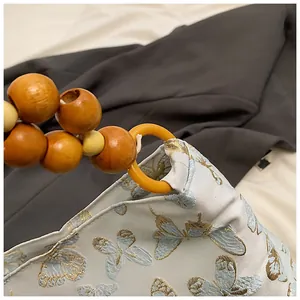 Detail einer hellblauen Tasche mit Schmetterlingsstickerei und Holzperlengriff
