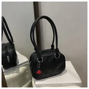 Dettaglio borsa in pelle nera con ciondolo a cuore rosso su superficie a specchio