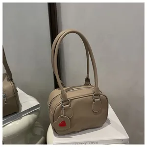 Dettaglio ravvicinato della borsa beige in pelle martellata con ciondolo a cuore