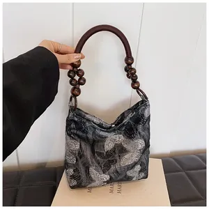 Detailaufnahme der schwarzen Tasche mit Schmetterlingsstickerei und Holzperlen-Tragegriff