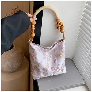 Detailaufnahme der lila Schmetterlingsstickerei auf weißem Canvas mit Holzperlengriffen