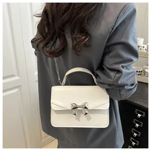 Détail d'un mini sac blanc avec nœud argenté et bandoulière chaîne porté par un mannequin