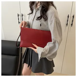Detail of red leather envelope clutch bag held by model wearing a striped shirt