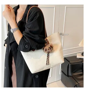 Close-up of white pebbled leather tote bag with brown straps and a leopard heart charm