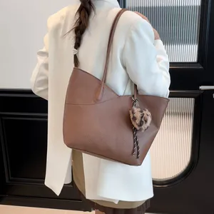 Brown lychee texture tote bag with leopard print pom-pom charm shown on a female model