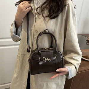 Sac Boston vintage marron foncé avec poignées et bandoulière porté avec un manteau