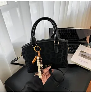 Dettaglio borsa nera con trama leopardata, ciondolo in legno e logo dorato JUHAI