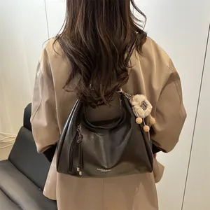 Elegant large capacity black leather shoulder bag with plush pendant on woman model